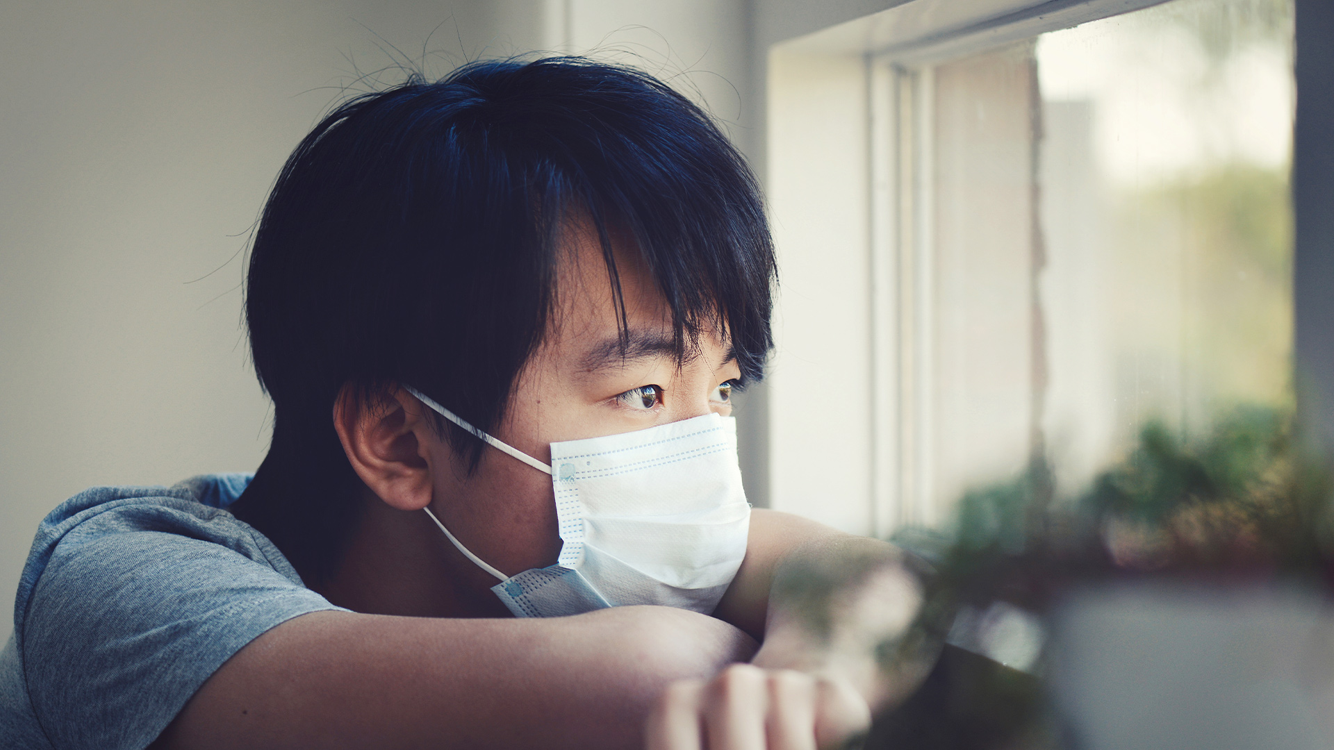 Young man wearing mask looking out a window
